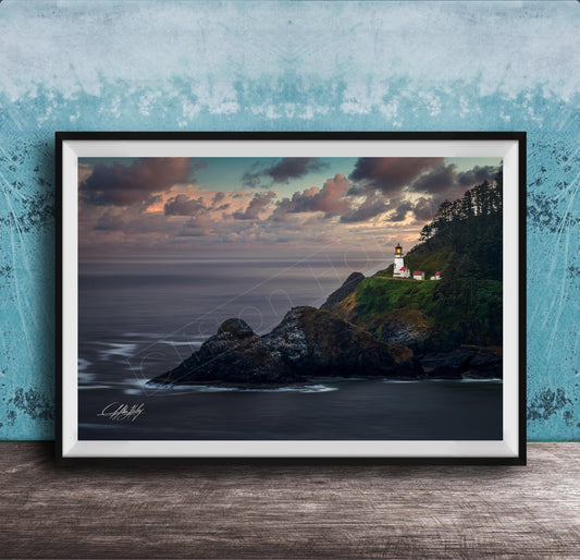 A framed photograph depicting a lighthouse on a cliff overlooking the ocean at sunset.