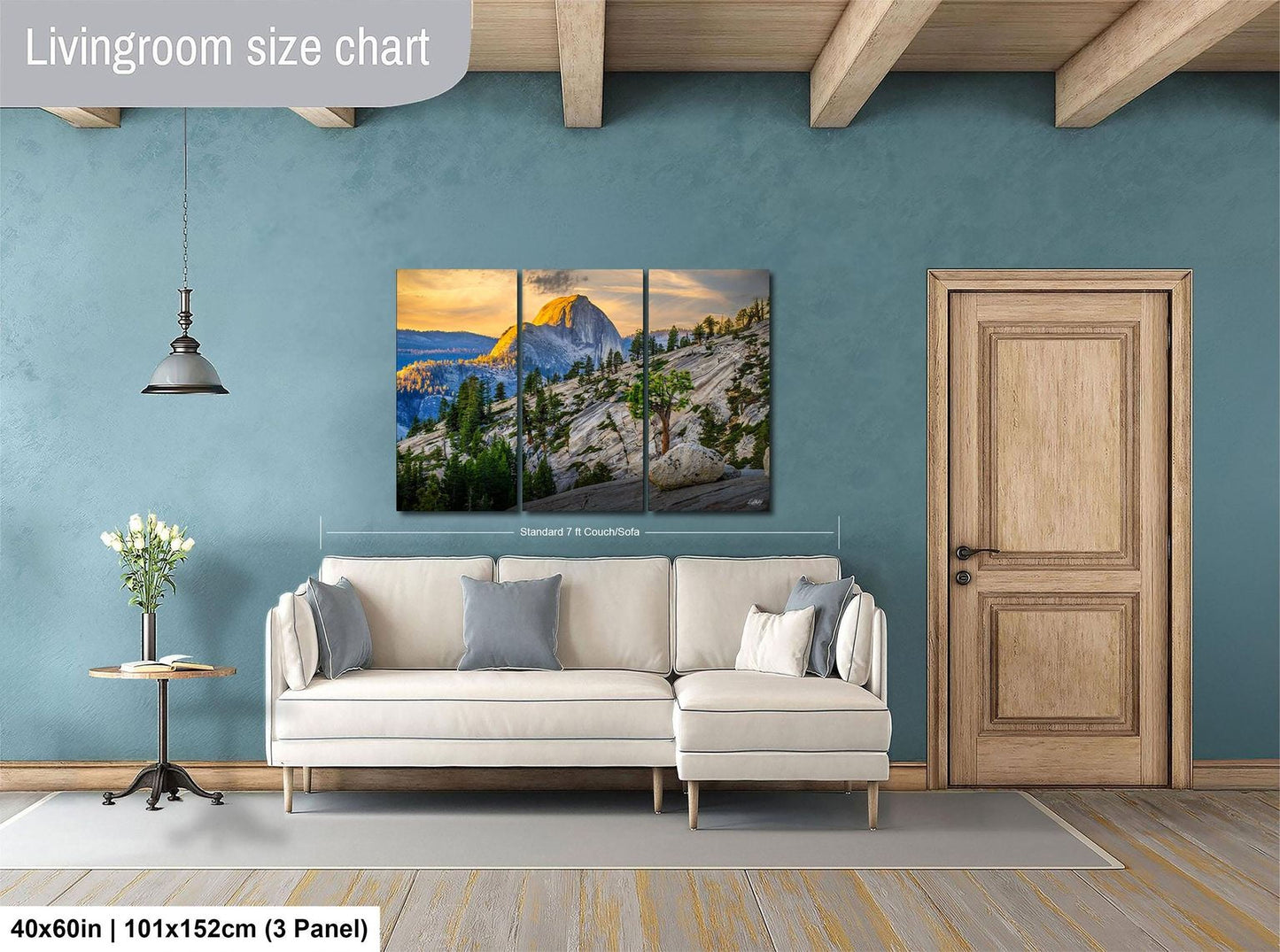 The image is a living room with a large, high-quality landscape painting hanging on the wall. The painting depicts a mountainous, forested scene with a sunset in the background. The room has a white sofa and a wooden door, creating a cozy and inviting atmosphere. The painting is approximately 40 inches wide and 101.5 inches tall, making it a prominent feature in the room.