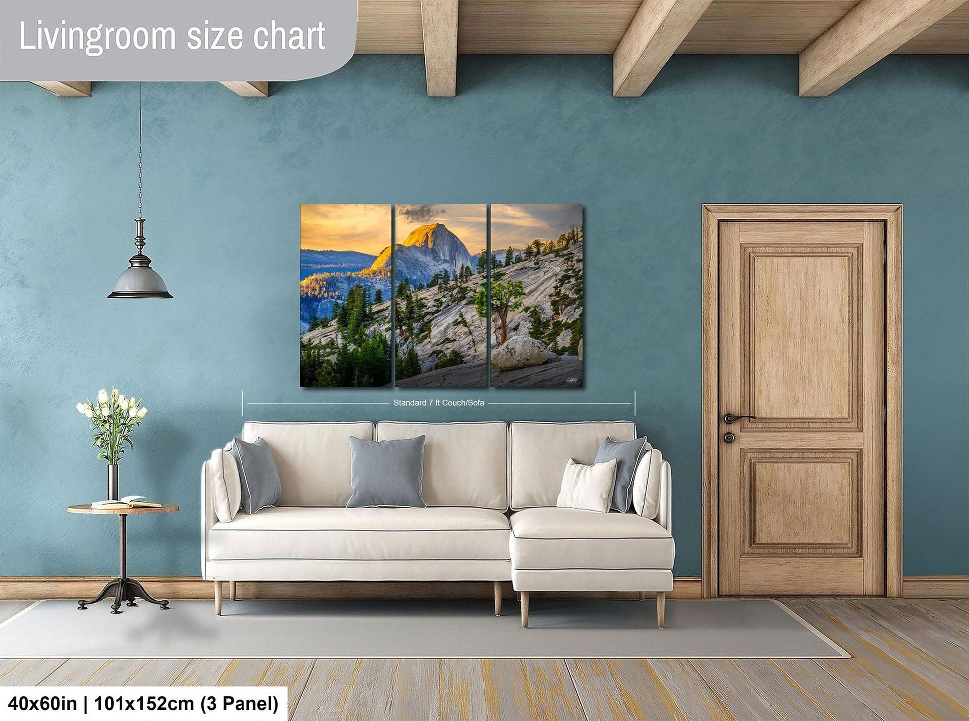 The image is a living room with a large, high-quality landscape painting hanging on the wall. The painting depicts a mountainous, forested scene with a sunset in the background. The room has a white sofa and a wooden door, creating a cozy and inviting atmosphere. The painting is approximately 40 inches wide and 101.5 inches tall, making it a prominent feature in the room.