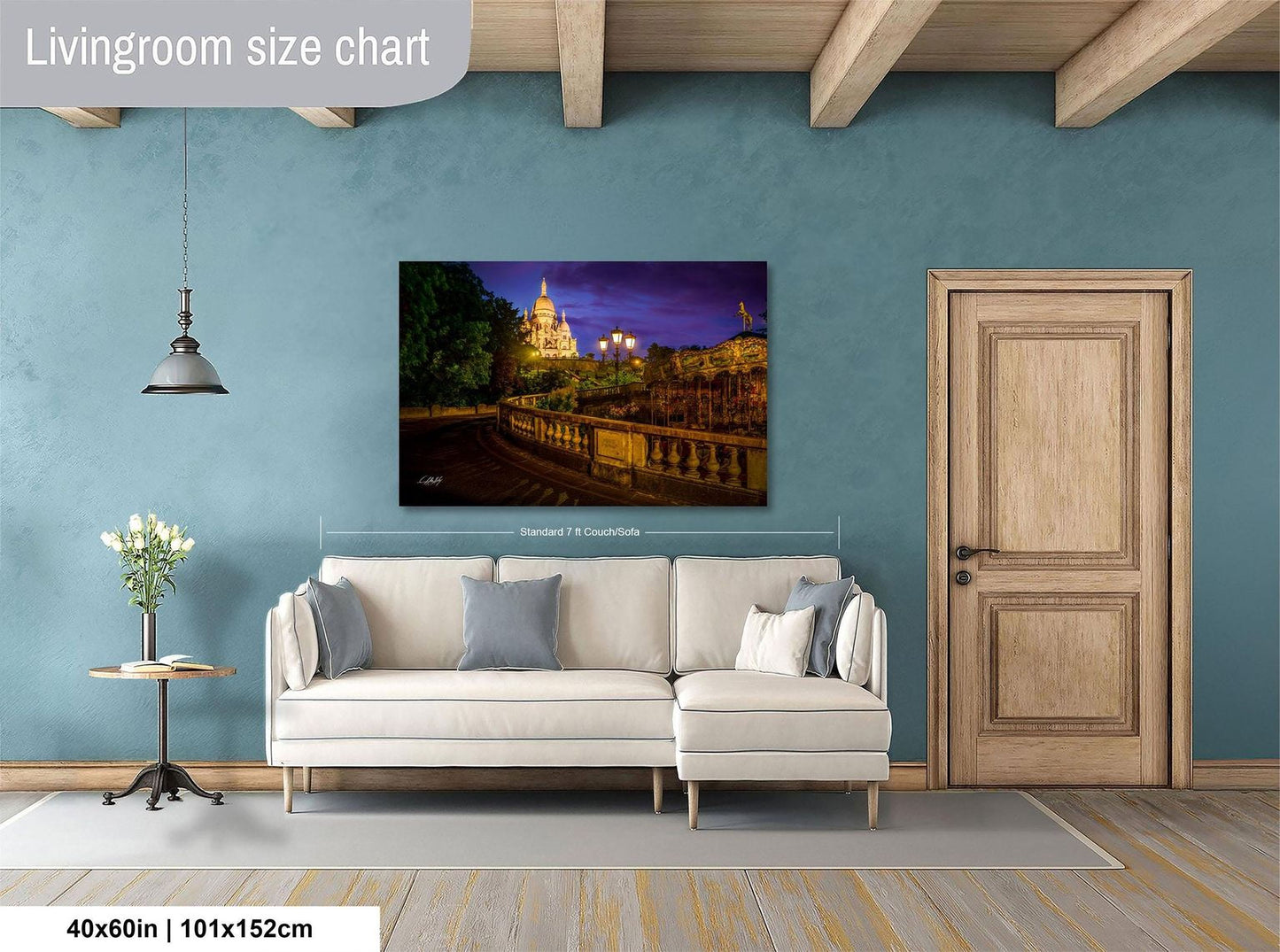 a living room with a large painting of a cityscape hanging on the wall. The painting is framed and measures 40 inches by 101.5 centimeters. The room has a white sofa, a wooden door, and a small table with a vase of flowers.