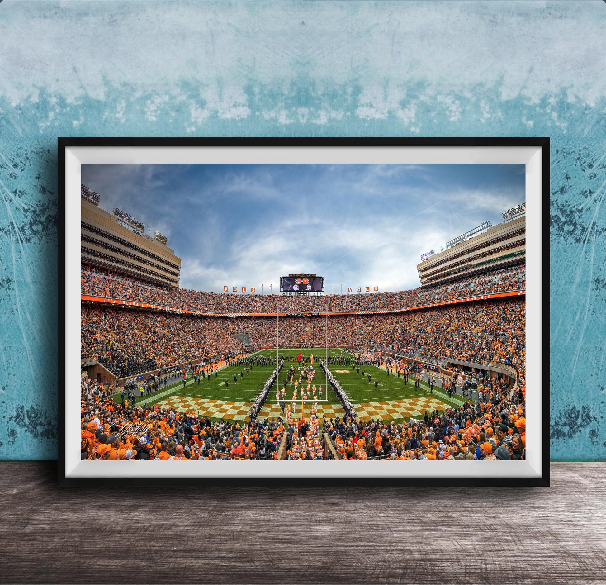 A framed photograph of a crowded football stadium during a game, with the field and stands filled with spectators.
