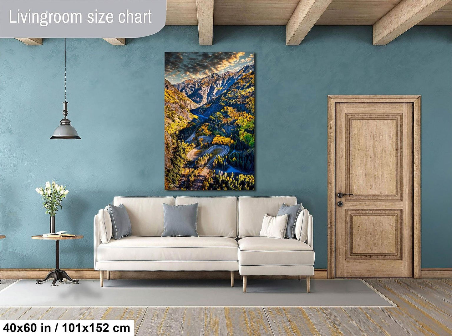a living room with a large, colorful painting of a mountainous landscape hanging on the wall. The painting is framed in a wooden frame and is approximately 40 inches wide and 51 inches tall. The room has a white sofa and a wooden door, creating a cozy and inviting atmosphere.