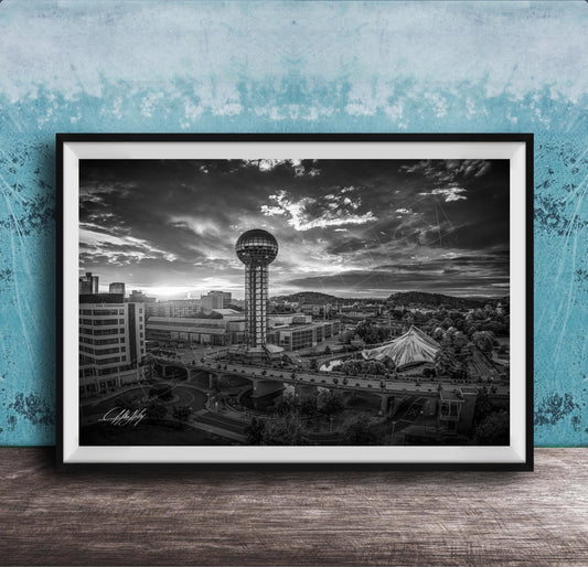 A black and white photograph of a cityscape, featuring a tall tower, a bridge, and other buildings, set against a cloudy sky.