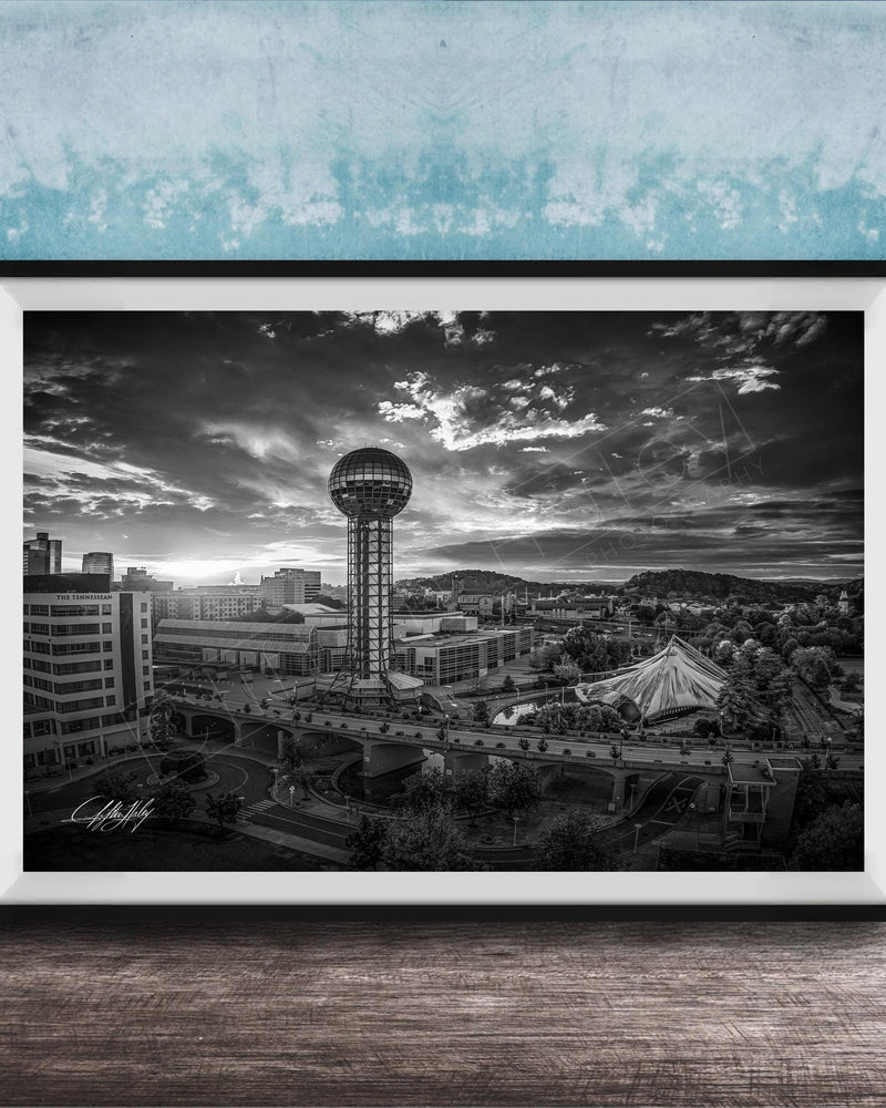 A black and white photograph of a cityscape, featuring a tall tower, a bridge, and other buildings, set against a cloudy sky.