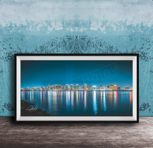 A framed photograph of a city skyline at night, with the buildings' lights reflected in the water below.