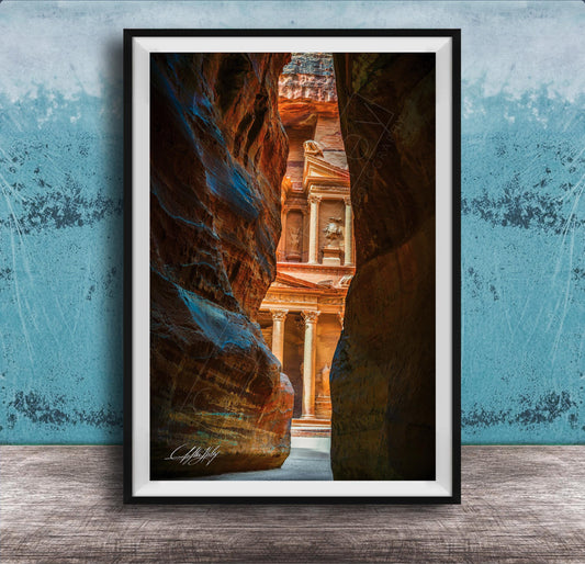 A framed photograph of a narrow passage between two large rock formations, with a building visible through the opening.