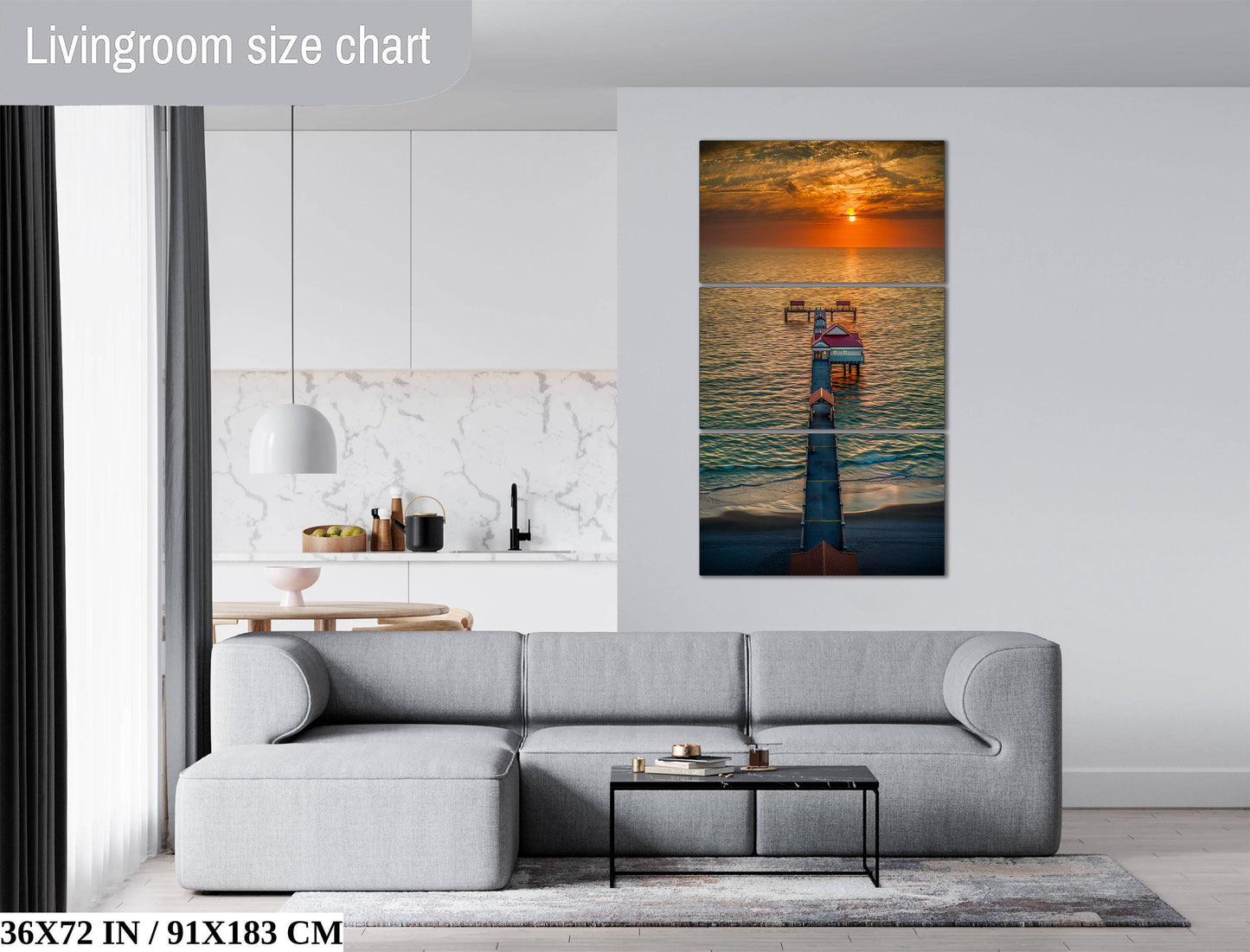The image is a living room with a gray sofa, a coffee table, and a large wall art depicting a sunset over the ocean.