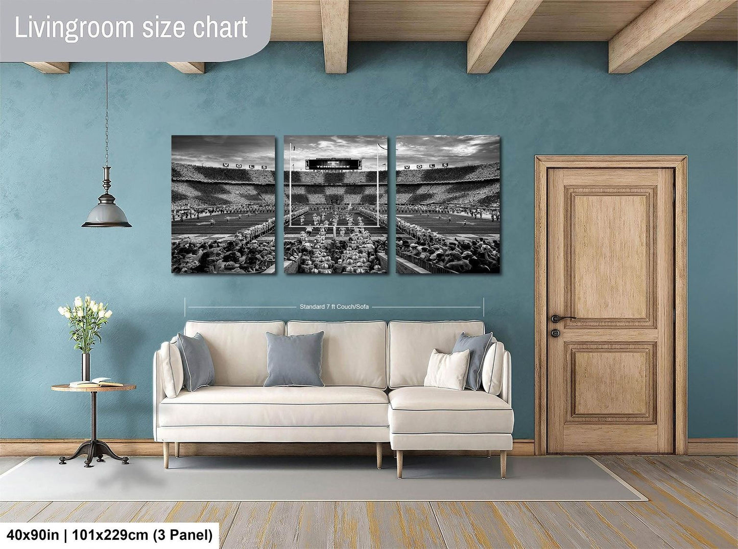 The image is a living room with a white sofa and a wooden door. Above the sofa, there is a large black and white photograph of a stadium, which appears to be a sports stadium. The photograph is divided into three panels, and the wall behind the sofa has a blue color. The living room is described as having a spacious and modern design, with a focus on the seating area and the large wall art.