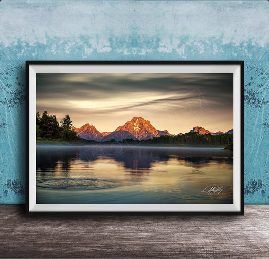 A framed photograph depicting a serene mountain landscape at sunset, with a calm lake reflecting the warm colors of the sky.