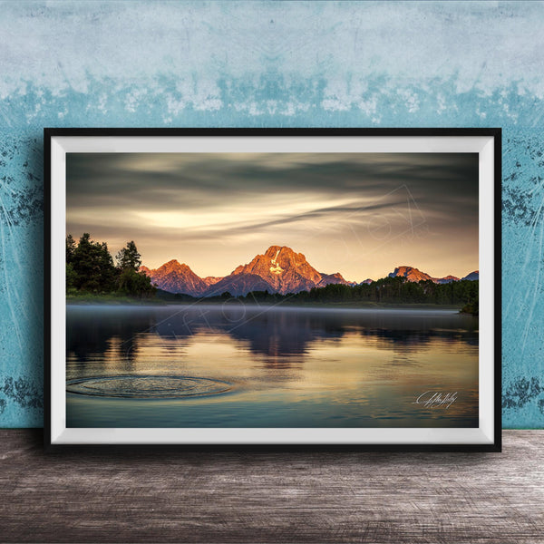 A framed photograph depicting a serene mountain landscape at sunset, with a calm lake reflecting the warm colors of the sky.