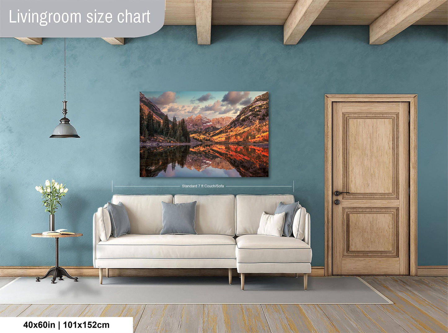 a living room with a large painting of a mountain landscape hanging on the wall. The painting is framed in white and measures 40 inches by 101.5 centimeters. The room has a white sofa and a wooden door, creating a cozy and inviting atmosphere.