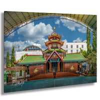 A colorful and ornate Chinese temple with a green roof and red walls, surrounded by trees and a large arched structure in the background.