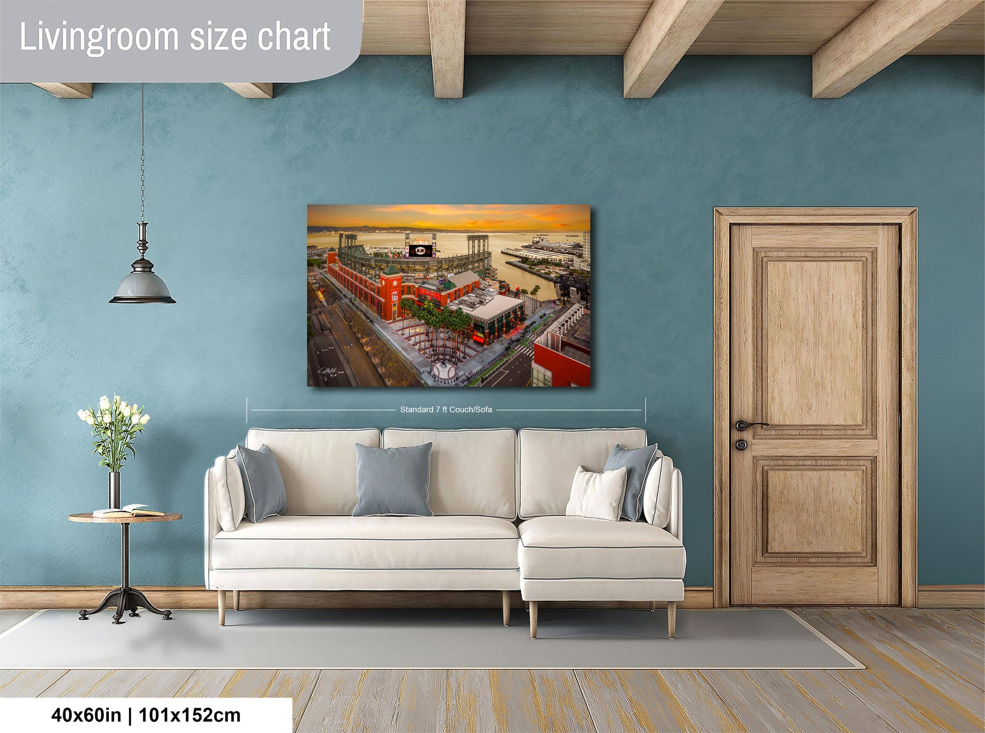 a living room with a large wall-mounted painting depicting a cityscape with a ferris wheel and buildings. The painting is framed and hangs above a white sofa with a wooden coffee table in front of it. The room has a wooden door and a wooden beam ceiling, creating a cozy and inviting atmosphere.