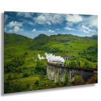 A steam train travels along a stone viaduct, surrounded by lush green hills and a blue sky with white clouds.