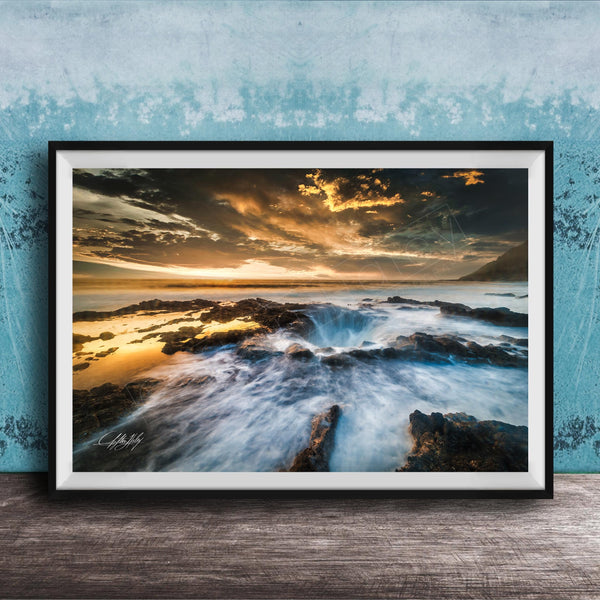 The image is a framed photograph of a rocky coastline with crashing waves, set against a dramatic sky with clouds and a sunset.