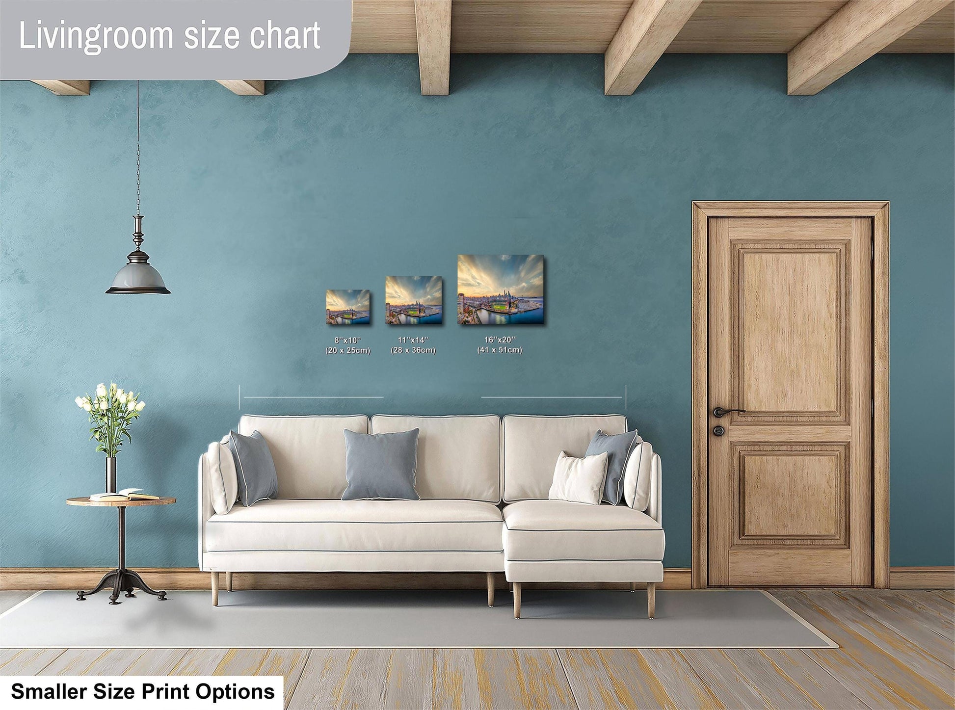 a living room with a white sofa, a wooden door, and a hanging light fixture. There are three paintings of different sizes displayed on the wall above the sofa.