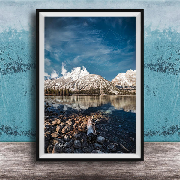 A framed photograph of a serene mountain landscape with a calm lake in the foreground, surrounded by snow-capped peaks and a clear blue sky.
