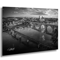 A black and white aerial view of a city with a large bridge spanning a river, with buildings and other structures visible in the background.