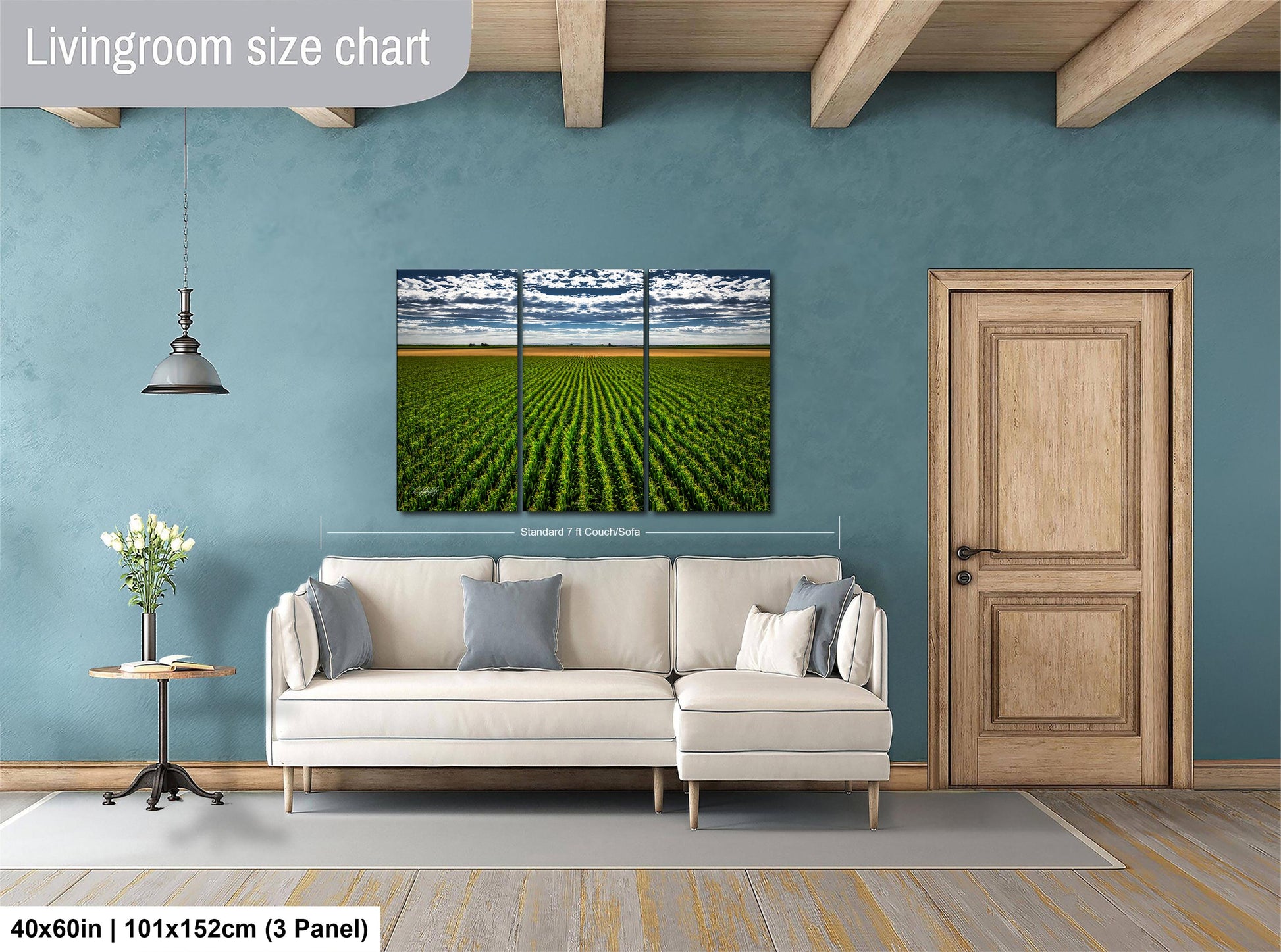 a living room with a large painting of a field of crops hanging on the wall. The painting is divided into three panels, and the living room has a white sofa and a wooden door.