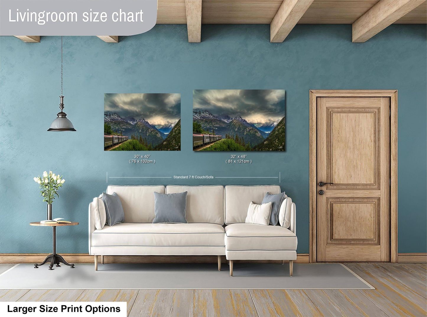 a living room with a white sofa and a wooden door. Above the sofa, there are two framed landscape paintings depicting mountains and a winding road. The paintings are of similar size, and the wall behind them is painted a light blue color.