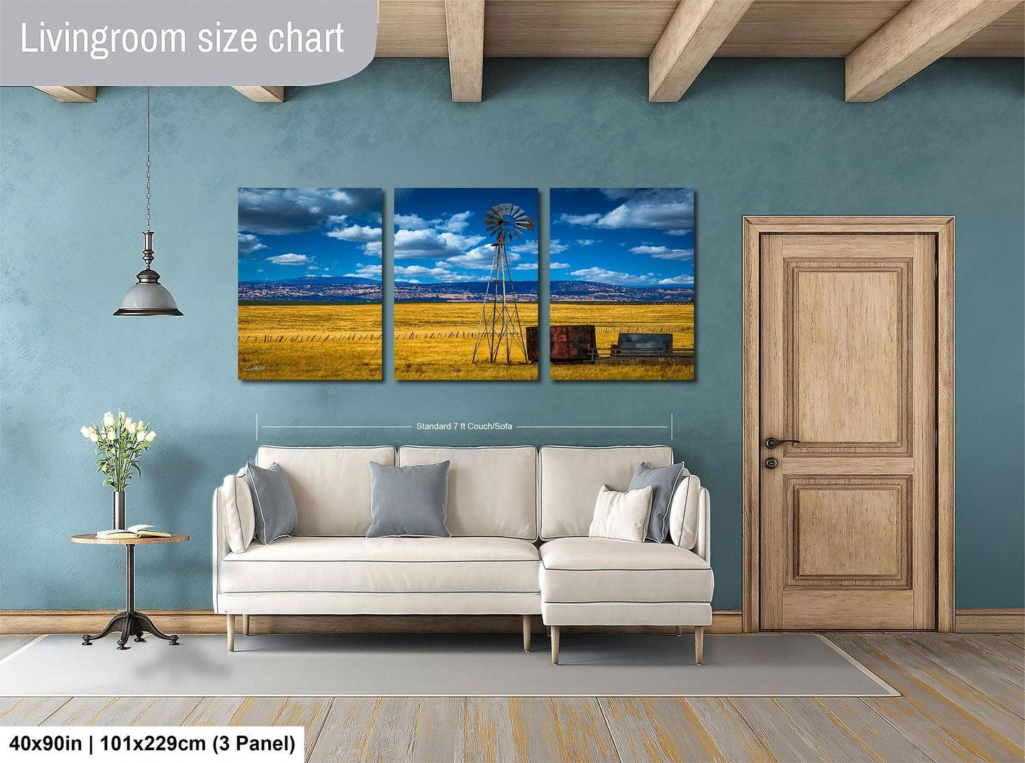 The image is a living room with a large living room size chart on the wall, featuring a three-panel landscape painting depicting a windmill and a field. The room has a white sofa, a wooden door, and a wooden floor.