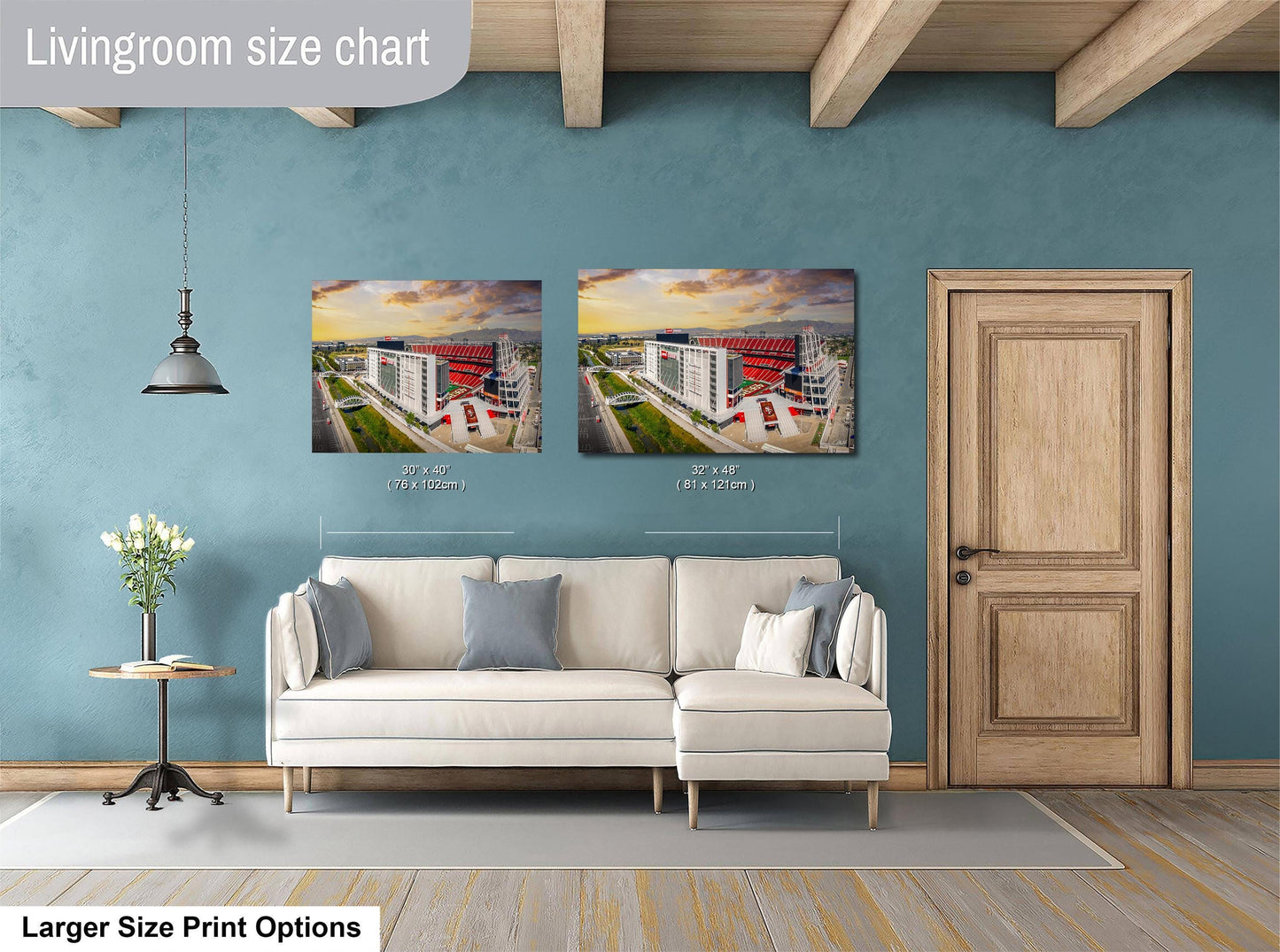 a living room with a white sofa and a wooden door. Above the sofa, there are two framed pictures of a building, likely a stadium. The living room has a blue wall and a wooden ceiling.