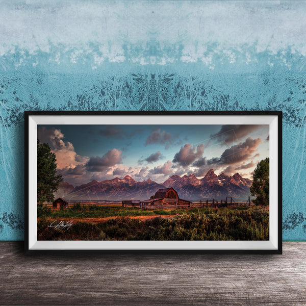 A framed photograph depicting a serene rural landscape with a barn, mountains, and a blue sky with clouds at sunset.