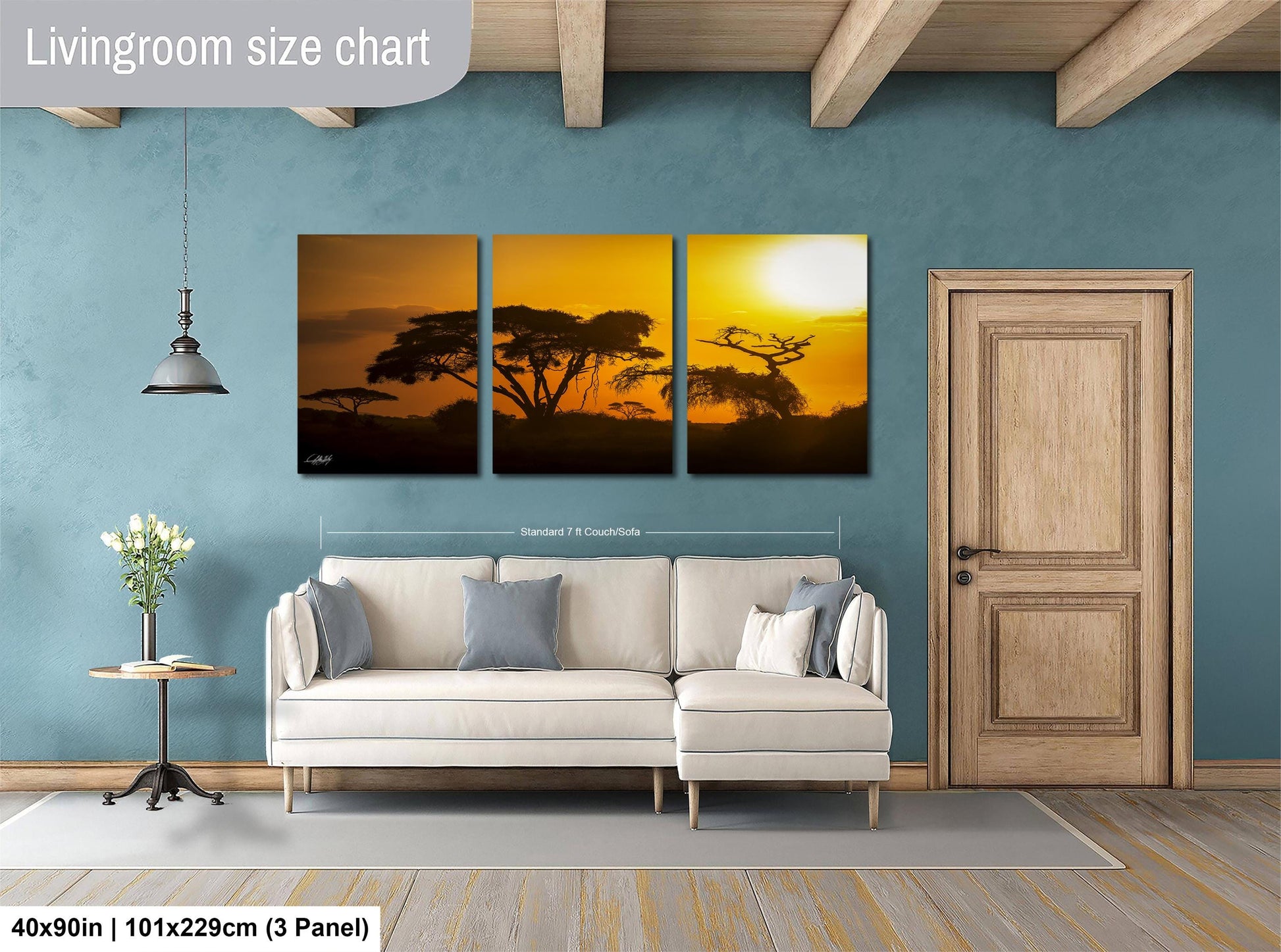 The image is a living room with a large wall art piece depicting a sunset over a landscape. The art piece is divided into three panels, each showing different aspects of the sunset. The living room has a white sofa and a wooden door, creating a cozy and inviting atmosphere.