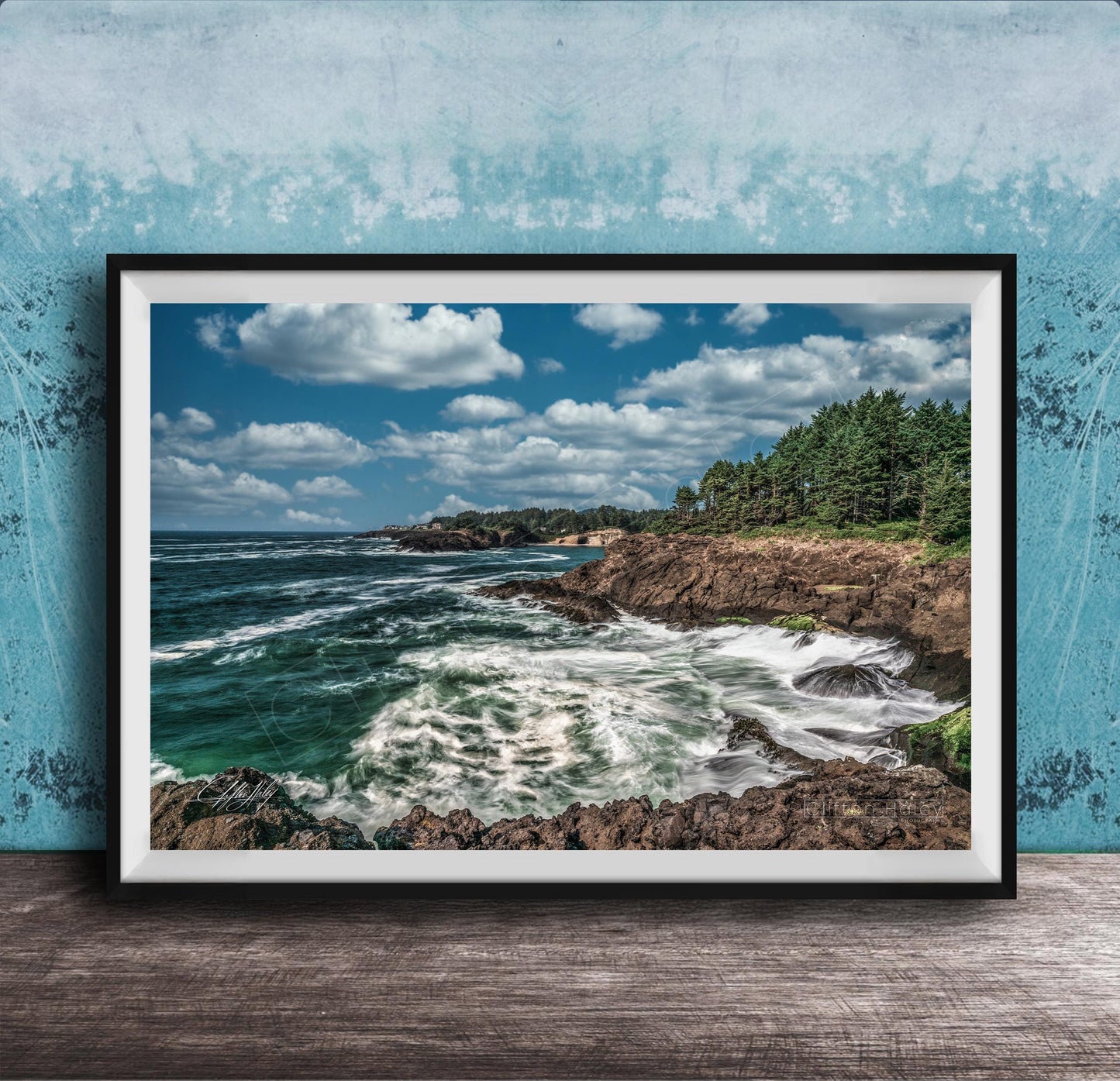 A framed photograph of a rocky coastline with crashing waves, set against a backdrop of a blue sky with fluffy white clouds.