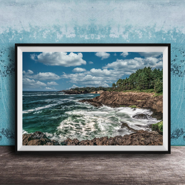 A framed photograph of a rocky coastline with crashing waves, set against a backdrop of a blue sky with fluffy white clouds.