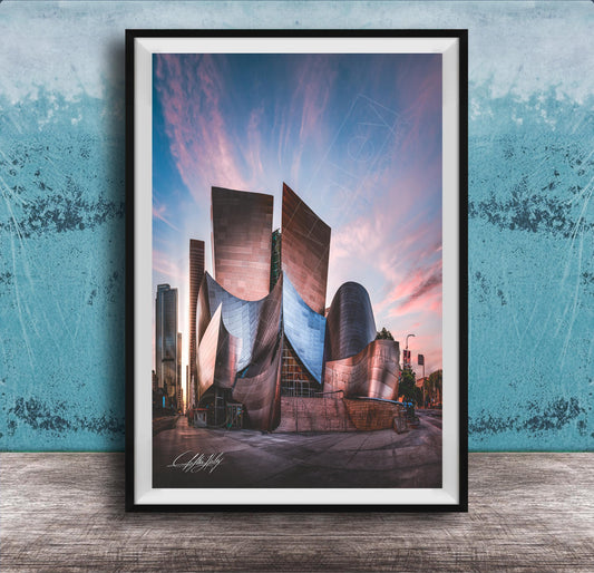 A framed photograph of a modern, curved building with a distinctive architectural design, set against a colorful sky at sunset.