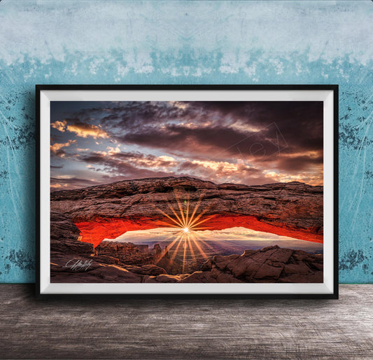 The image is a framed photograph depicting a dramatic sunset over a rocky landscape, with the sun's rays shining through the arch.