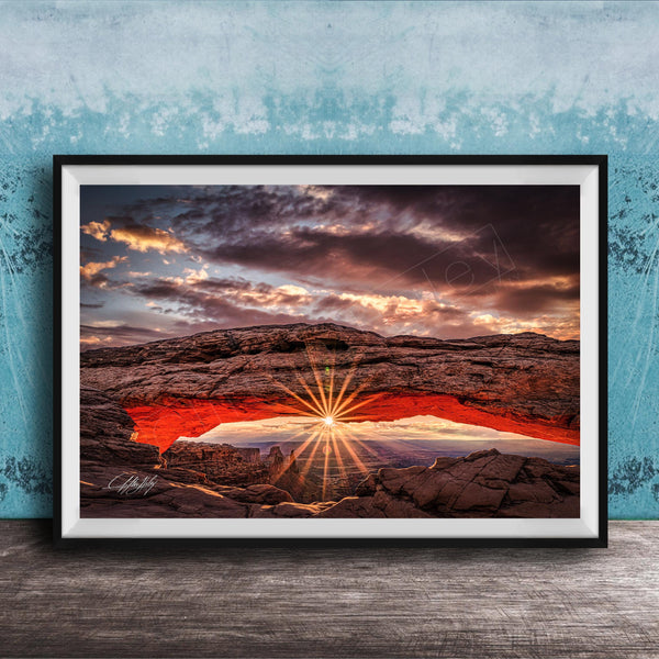 The image is a framed photograph depicting a dramatic sunset over a rocky landscape, with the sun's rays shining through the arch.