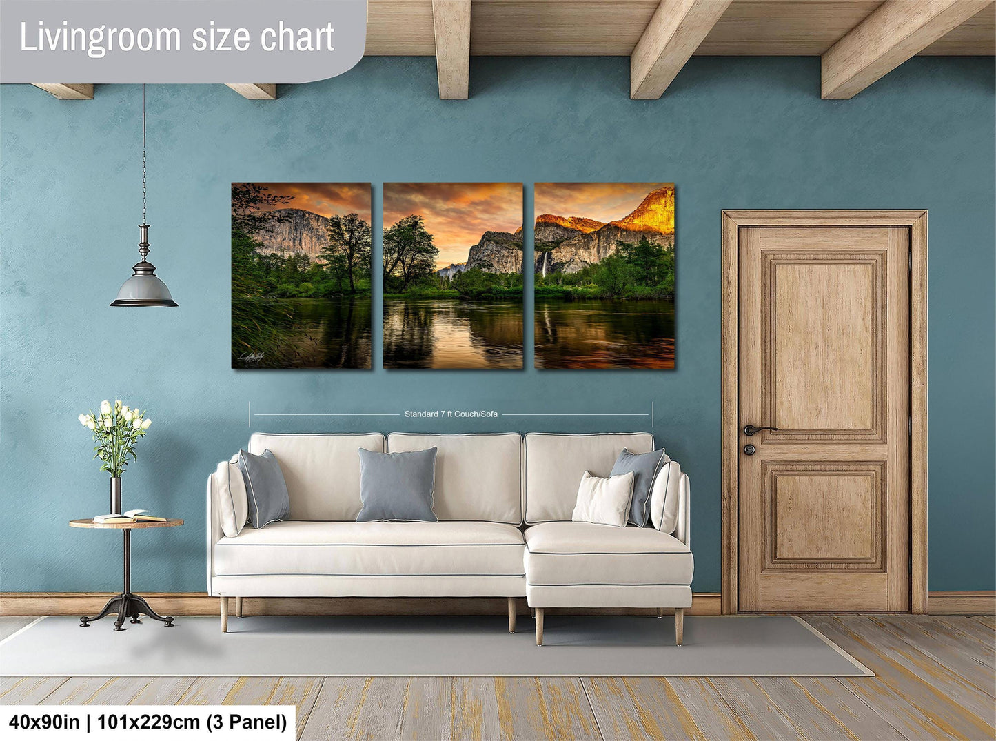 The image is a living room with a large wall art panel depicting a scenic landscape with mountains, trees, and a lake. The panel is divided into three sections, each showcasing a different part of the landscape. The living room has a white sofa and a wooden door, creating a cozy and inviting atmosphere.