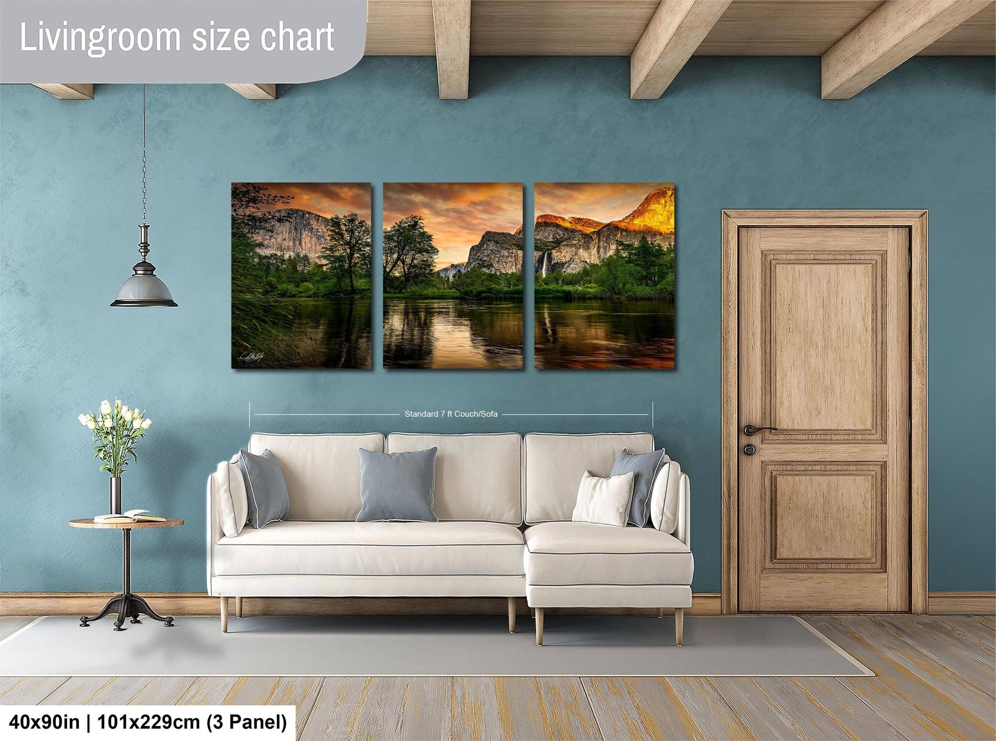 The image is a living room with a large wall art panel depicting a scenic landscape with mountains, trees, and a lake. The panel is divided into three sections, each showcasing a different part of the landscape. The living room has a white sofa and a wooden door, creating a cozy and inviting atmosphere.