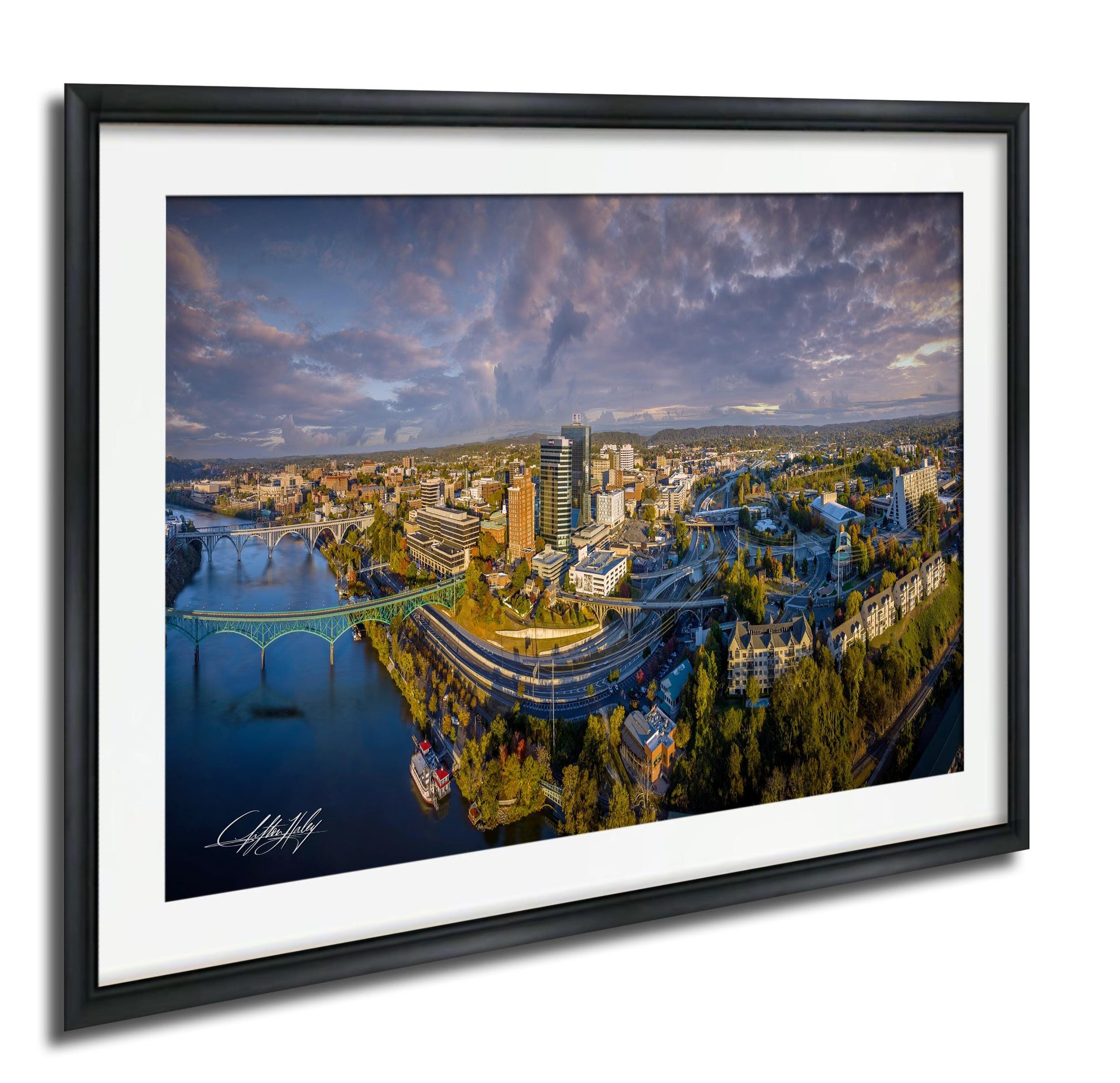 The image is a framed aerial view of a cityscape, featuring a bridge, buildings, and a river.