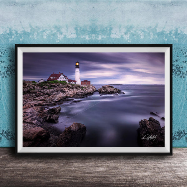 A framed photograph of a lighthouse on a rocky shore, with the ocean and a cloudy sky in the background.