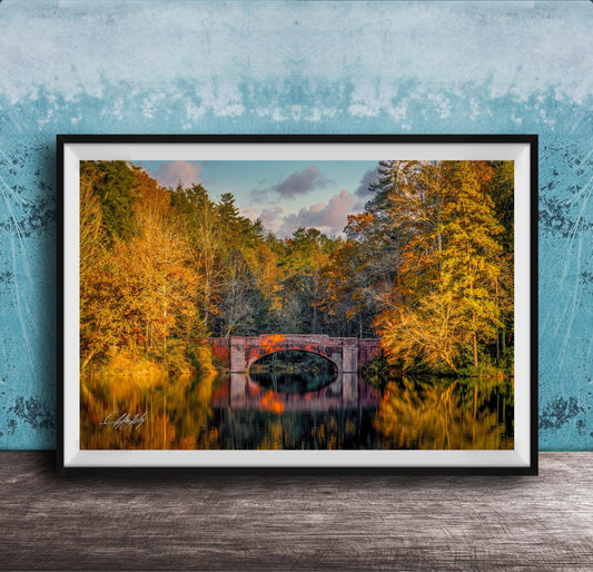 A framed photograph depicting a scenic autumn landscape with a red brick bridge spanning a tranquil lake, surrounded by vibrant fall foliage.