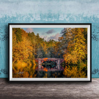 A framed photograph depicting a scenic autumn landscape with a red brick bridge spanning a tranquil lake, surrounded by vibrant fall foliage.
