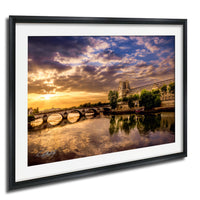 a picturesque scene of a bridge spanning a river, with the sun setting in the background, creating a beautiful reflection on the water's surface.