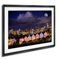 a cityscape at night, with a full moon illuminating the skyline and a row of houses with their lights on in the foreground.