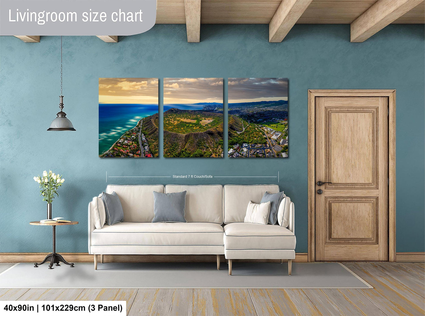 The image is a living room with a large wall-mounted painting depicting a scenic coastal landscape with mountains and a beach. The painting is divided into three panels, each showcasing different aspects of the landscape. The room has a white sofa and a wooden door, creating a cozy and inviting atmosphere.