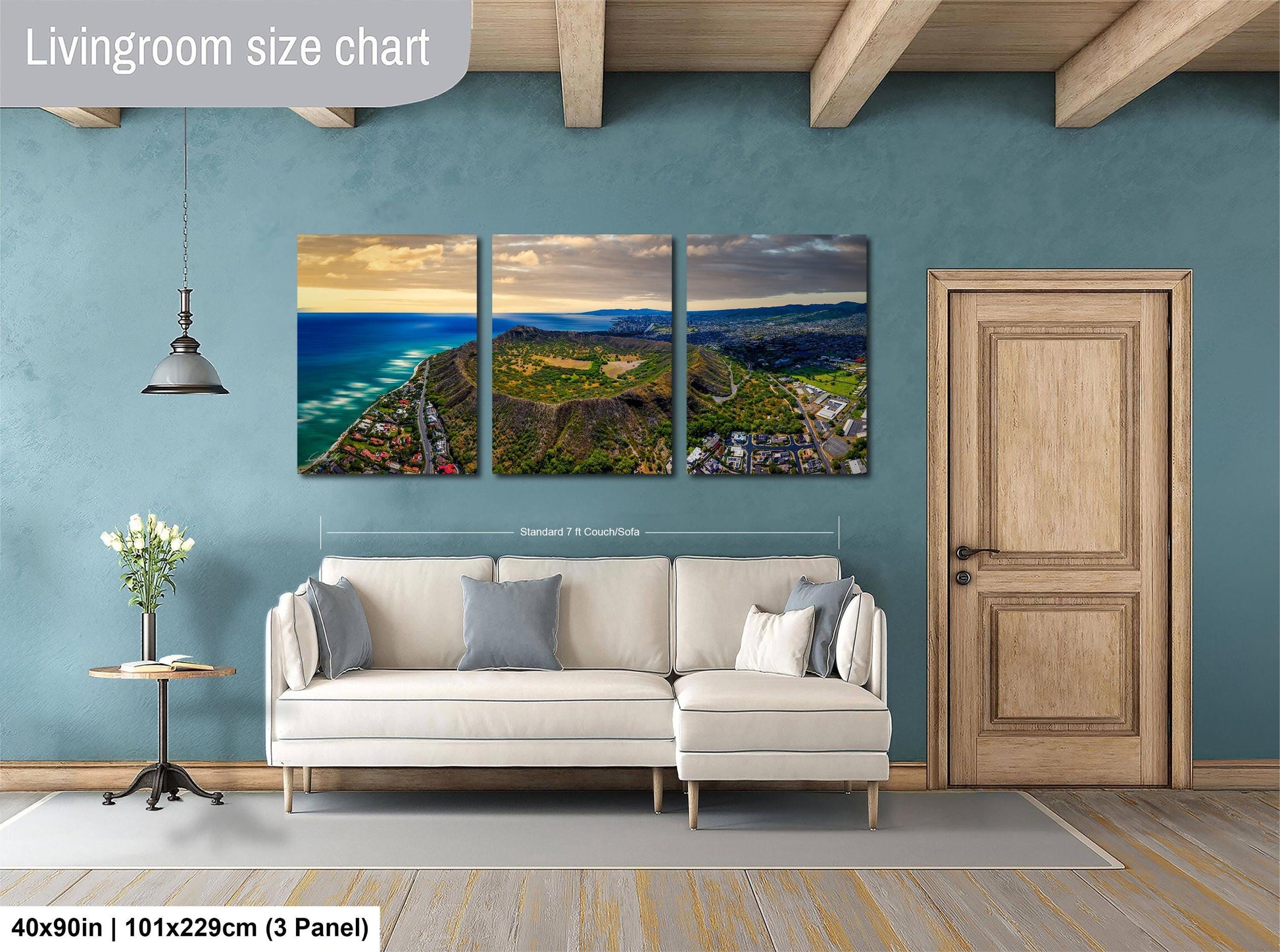 The image is a living room with a large wall-mounted painting depicting a scenic coastal landscape with mountains and a beach. The painting is divided into three panels, each showcasing different aspects of the landscape. The room has a white sofa and a wooden door, creating a cozy and inviting atmosphere.