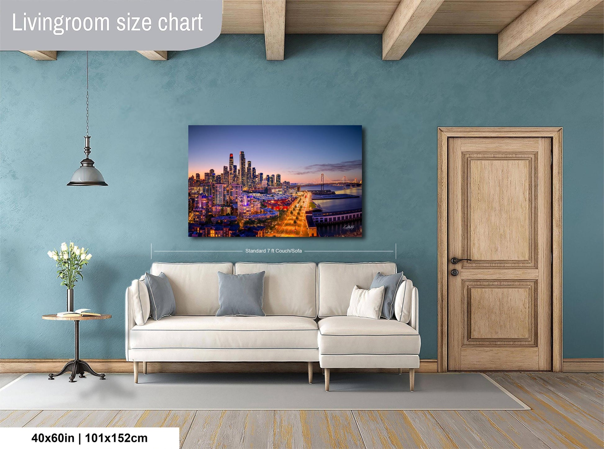 a living room with a large city skyline painting hanging on the wall. The painting is framed and measures 40 inches by 101.5 centimeters. The room has a white sofa and a wooden door, creating a cozy and modern atmosphere.