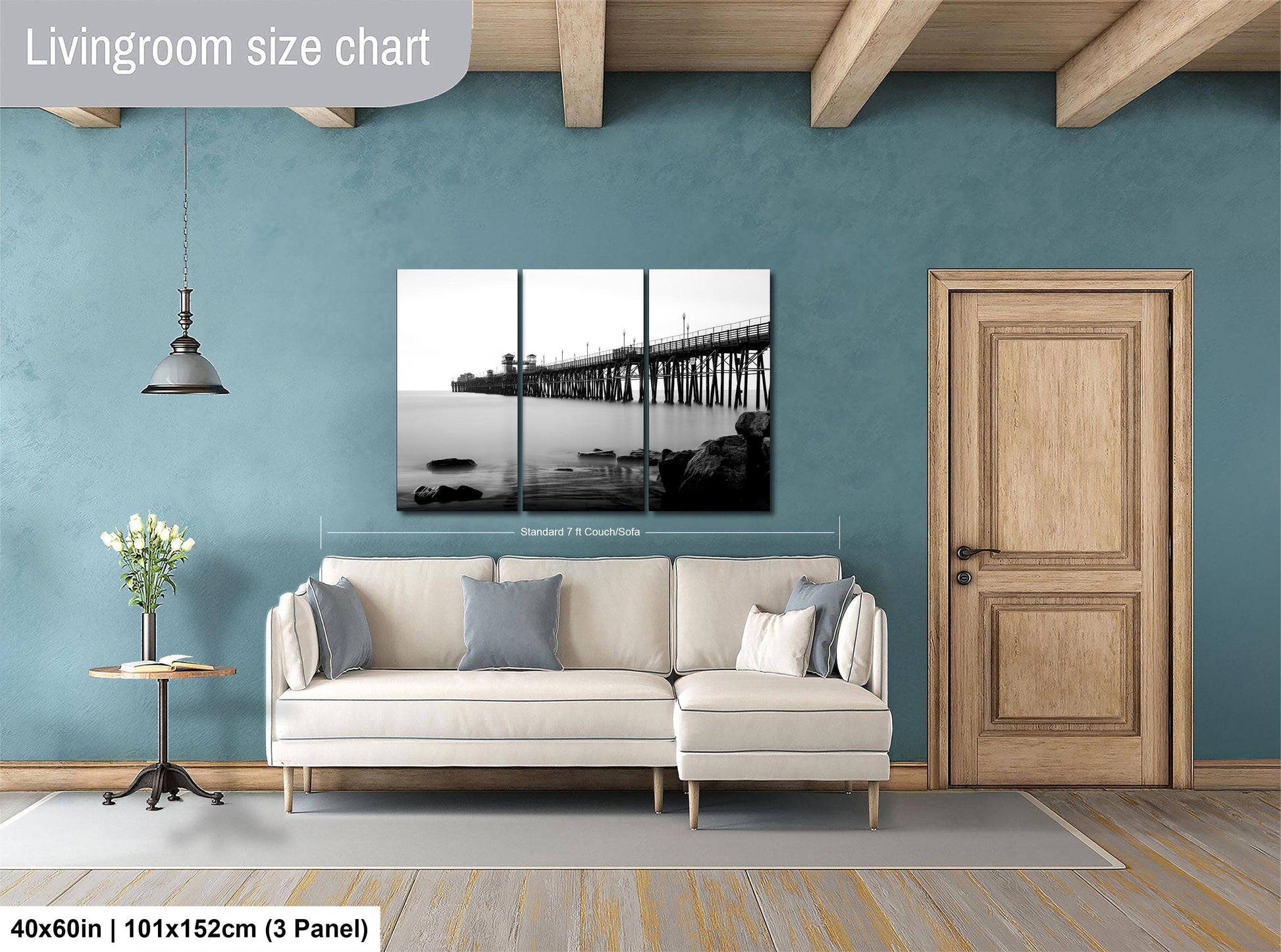 The image is a living room with a large white sofa, a wooden door, and a wall-mounted black and white photograph of a bridge. The room has a blue wall and a wooden floor.