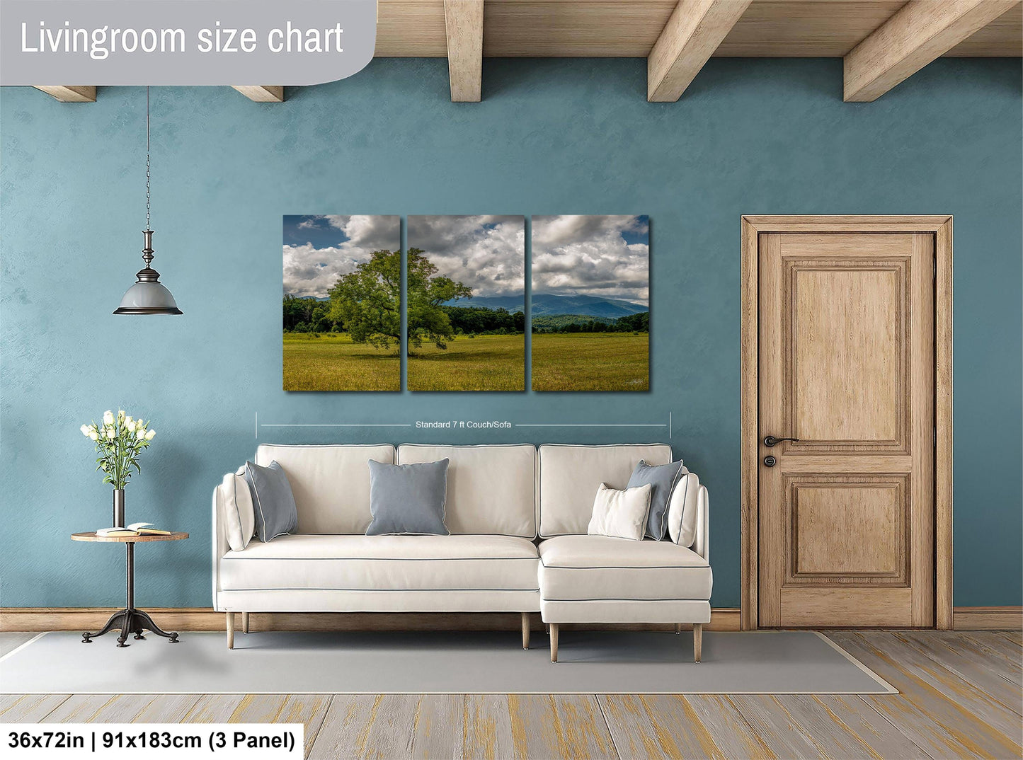 The image is a living room with a large white sofa, a wooden door, and a painting of a field with trees hanging on the wall.
