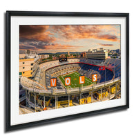 a large sports stadium with a field, surrounded by buildings and a cloudy sky in the background.