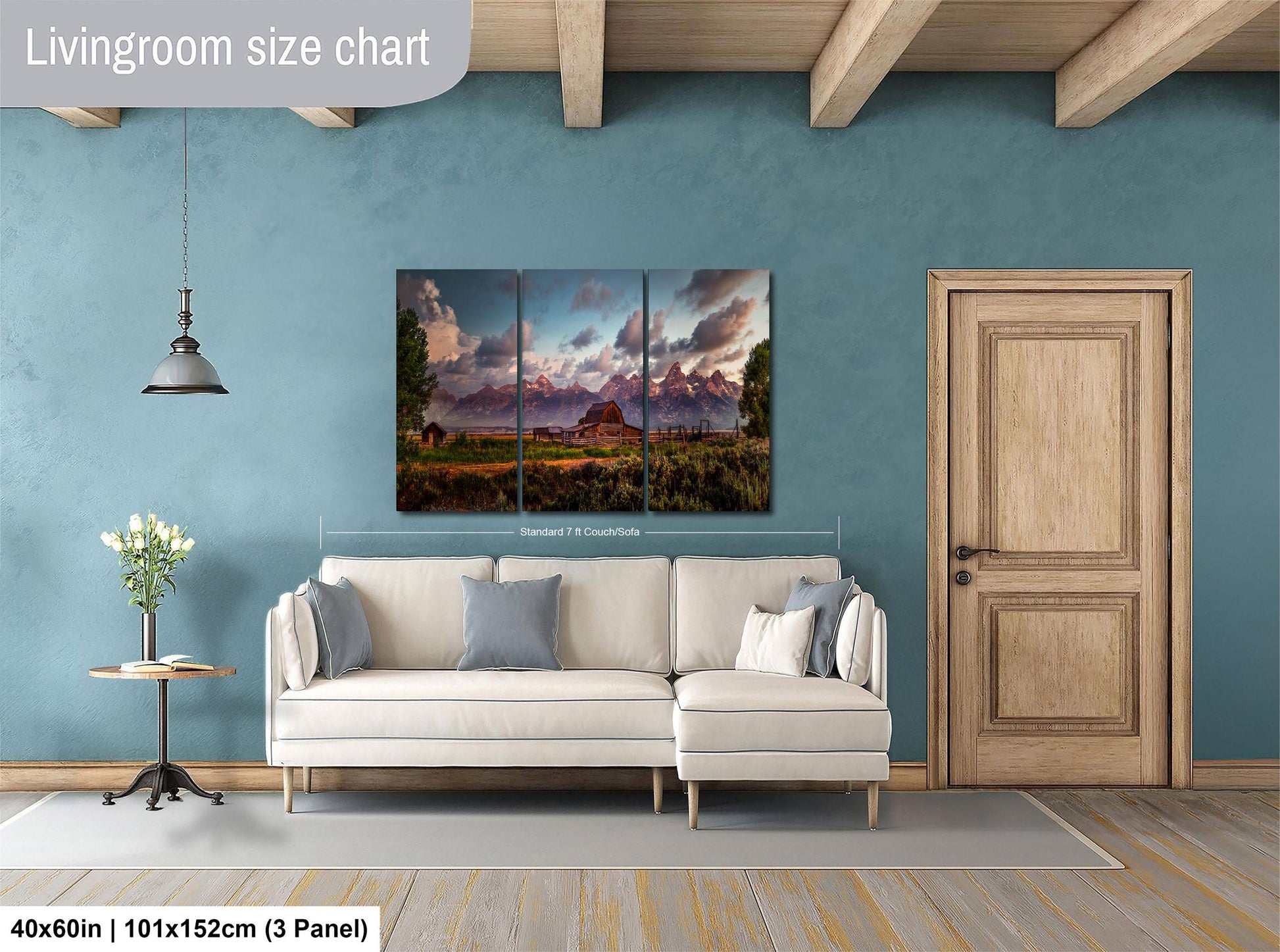 The image is a living room with a large painting of a mountain landscape hanging on the wall. The painting is divided into three panels, and the living room has a white sofa, a wooden door, and a small table with a vase of flowers.