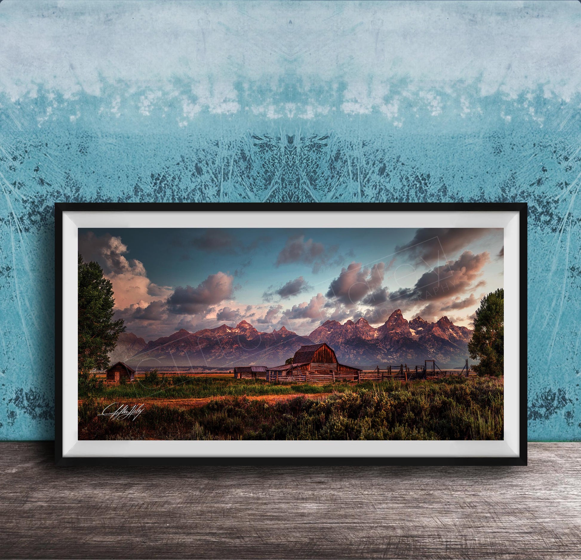 A framed photograph depicting a serene rural landscape with a barn, mountains, and a blue sky with clouds at sunset.