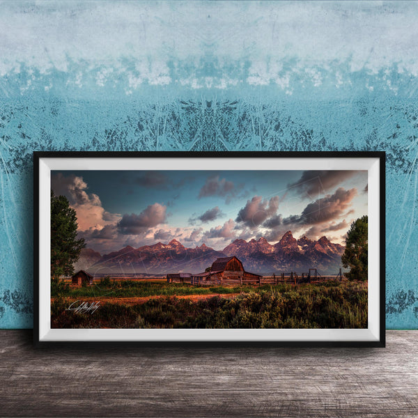 A framed photograph depicting a serene rural landscape with a barn, mountains, and a blue sky with clouds at sunset.